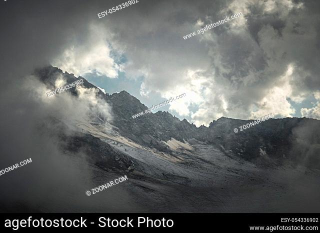 Mountain landscape of a high mountain slope with a cracked glacier muddy volcanic slope against the backdrop of the Caucasus Mountains in the window of clouds