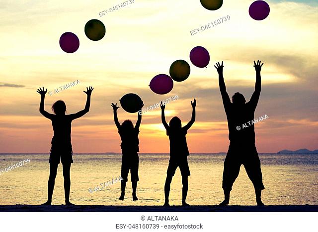 Father and children with balloons playing on the beach at the sunset time. People having fun on the beach. Concept of friendly family and of summer vacation