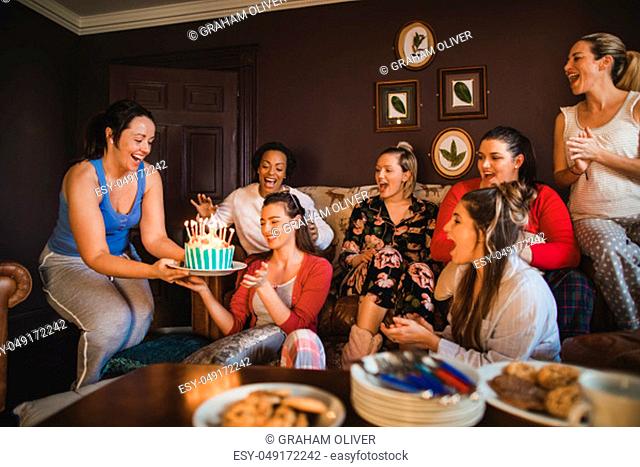 Small group of female friends celebrating a birthday with a Birthday cake while relaxing at home