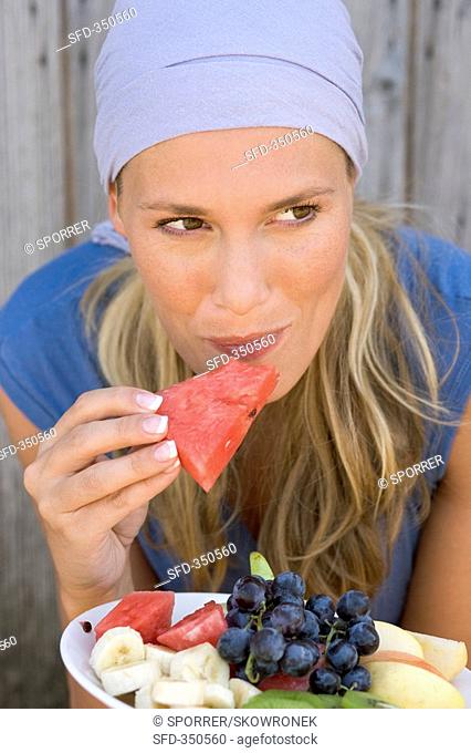 Woman eating watermelon from a plate of fruit