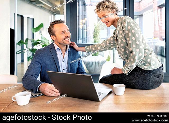 Happy business colleagues discussing over laptop in office cafeteria