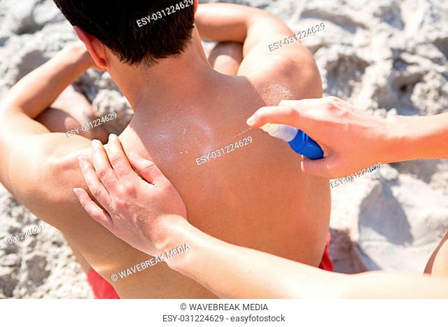 Woman applying spray on man back at beach