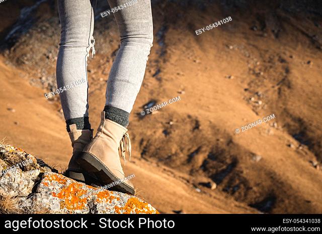 Close-up of female legs in stylish mountain boots standing on the top of a cliff on the background of a mountain slope