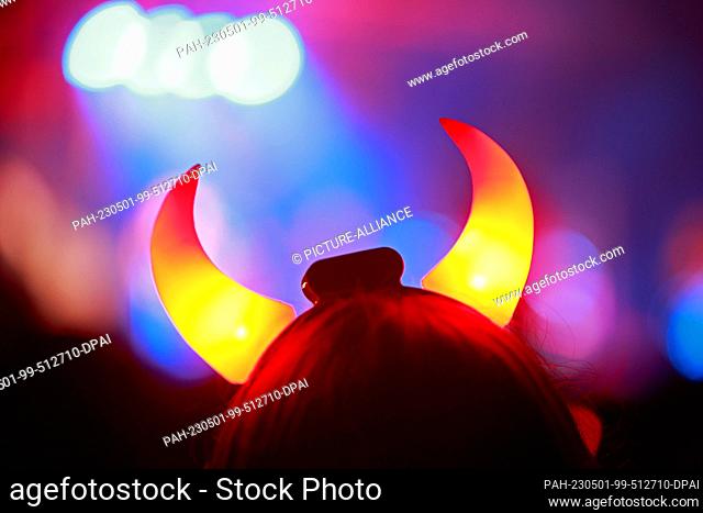 30 April 2023, Saxony-Anhalt, Schierke: With illuminated devil horns, a visitor of the Walpurgis festival in Schierke stands in front of a stage