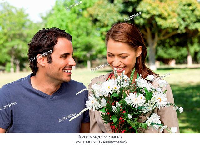 Woman happily looking into a bunch flowers as she is being watched by her friend