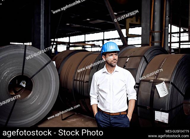 Male owner contemplating with hands in pockets standing in factory