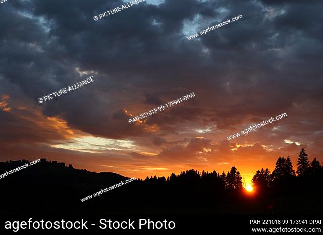 18 October 2022, Bavaria, Oy-Mittelberg: The sun setting behind a forest colors the partly cloudy sky in shades of red. Photo: Karl-Josef Hildenbrand/dpa