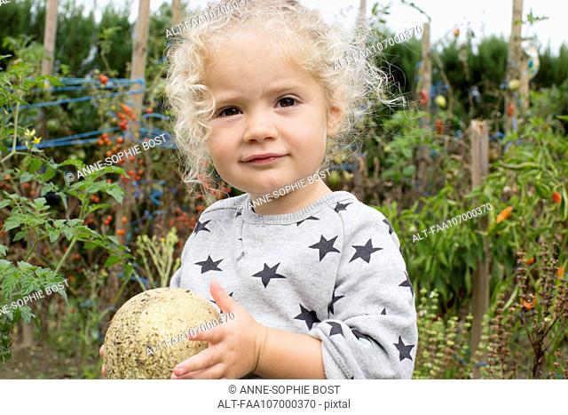 Little girl with cantaloupe in garden