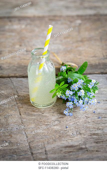 Rhubarb lemonade in a mini glass bottle next to a bouquet of forget-me-nots