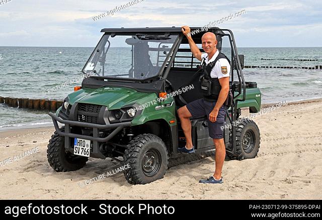 12 July 2023, Mecklenburg-Western Pomerania, Warnemünde: At a press event, Stefan Bischoff, beach bailiff, stands with his buggy on the Baltic Sea beach