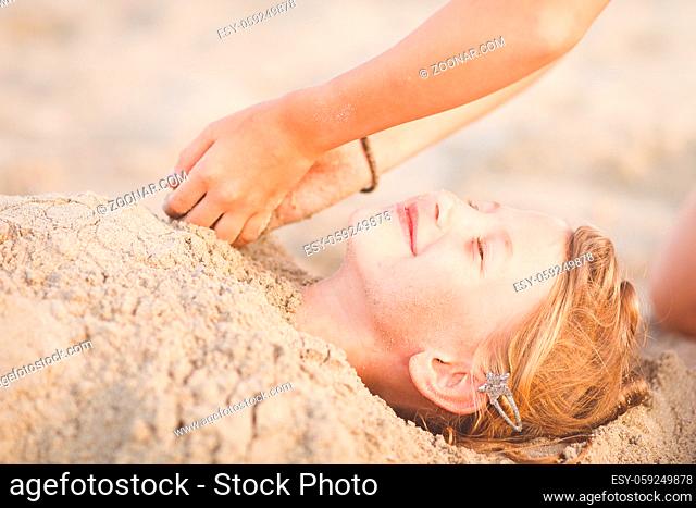 Two hands digging young girl in the sand at the beach