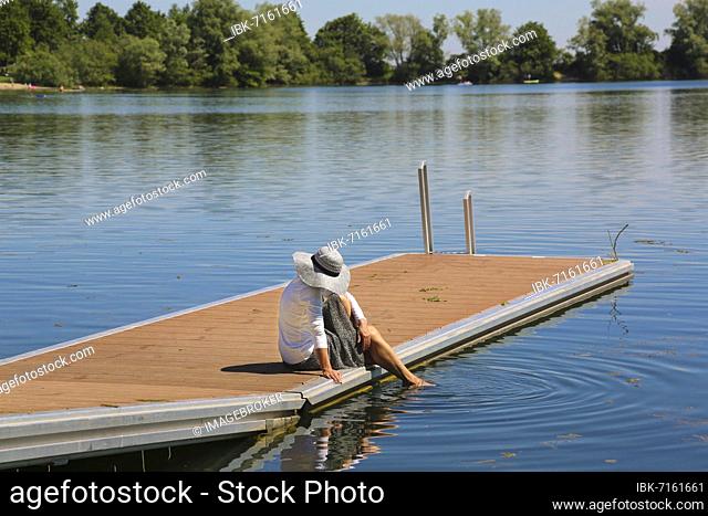 Woman with sun hat on jetty, one leg in water, Ludwigsfelder See, bathing lake, body of water, Neu-Ulm, Bavaria, Germany, Europe