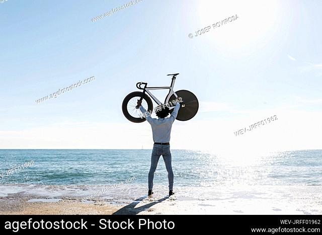 Man lifting his bike on the beach, watching the sea