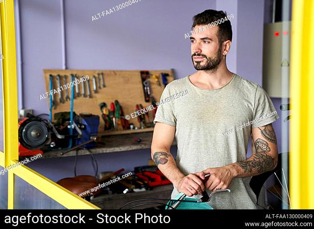 Medium-shot of bearded mechanic standing in his workshop in front of his tools