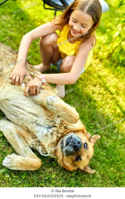 Cute girl and old dog enjoy summer day on the grass in the park. Child and animals on the backyard at home, happy. Love pets