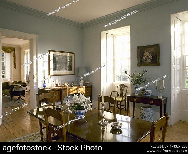 A green county dining room with polished oak table, chairs, side board, bay windows
