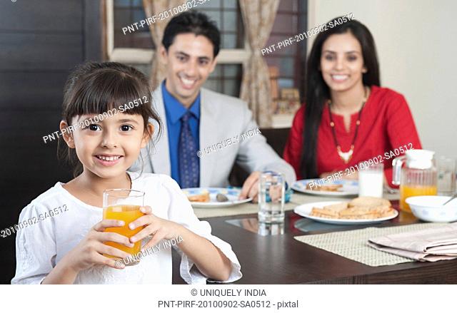Portrait of a girl holding a glass of juice with her parents in the background