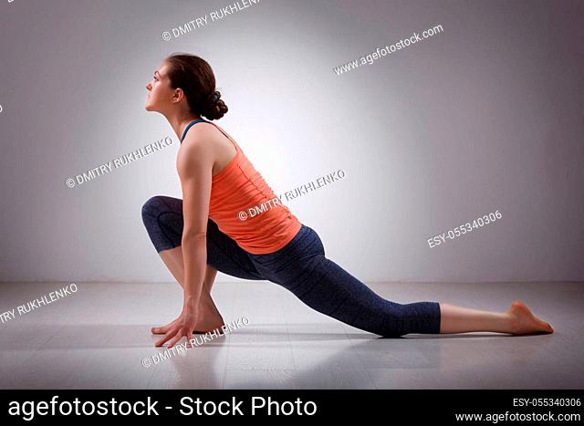 Beautiful sporty fit yogini woman practices yoga asana Anjaneyasana - low crescent lunge pose in surya namaskar in studio