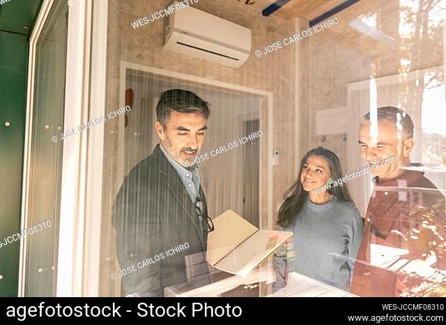 Real estate agent discussing purchase contract with new home owners standing at window