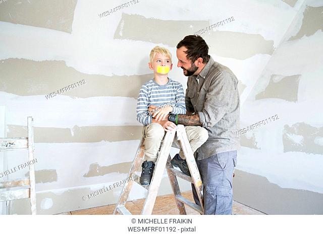 Father looking at son on ladder with taped mouth