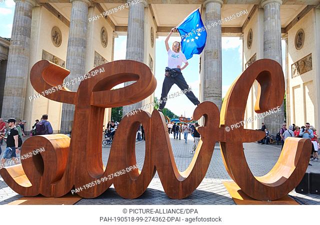 18 May 2019, Berlin: The artist Mia Florentine Weiss stands on her sculpture ""Love Hate"" in front of the Brandenburg Gate and waves the European flag