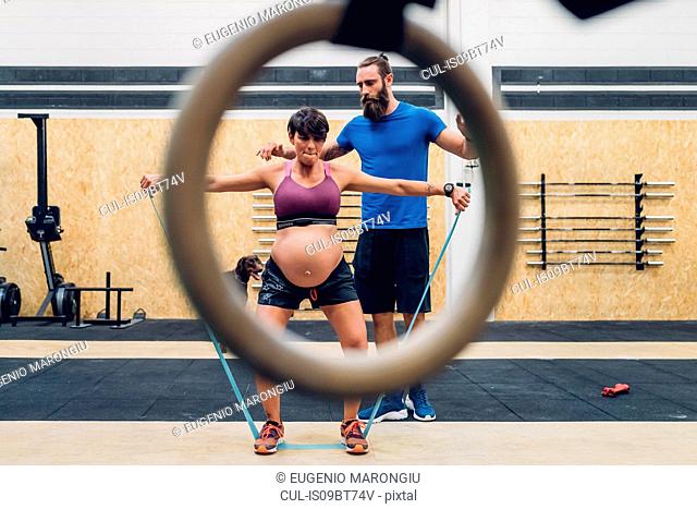 Trainer guiding pregnant woman using ropes in gym