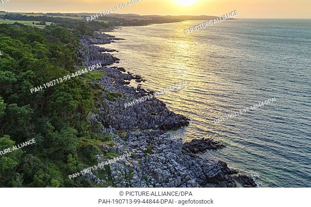 30 June 2019, Denmark, Randklöve: Sunset over the rocky coast of the Randklöven on the north coast of the Danish Baltic Sea island (aerial view with a drone)