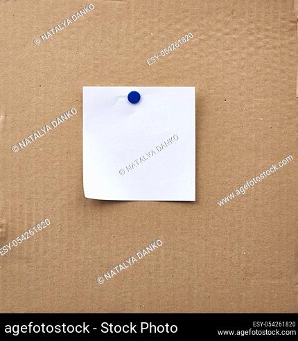 blank square white sheet of paper attached with an iron button on a brown cardboard surface. Design template