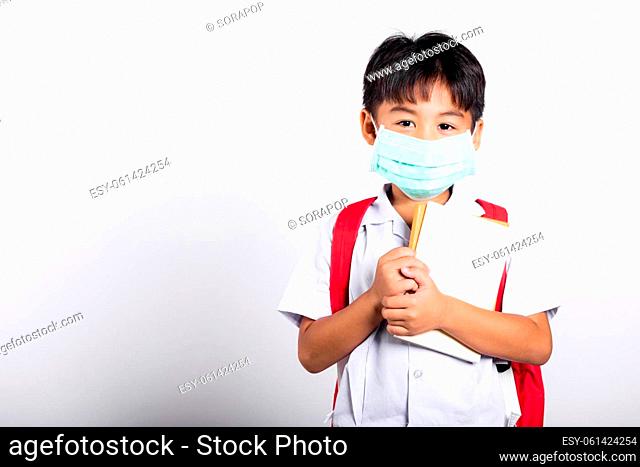 Asian student kid boy wearing student thai uniform and medical protect face mask and hugging note book in studio shot isolated on white background