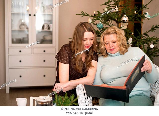 Two women looking photo album near a Christmas tree. Mother with daughter