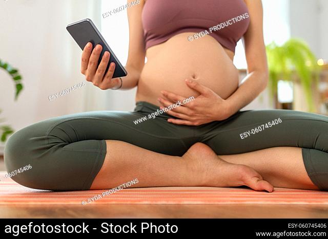 close up of pregnant woman with phone doing yoga