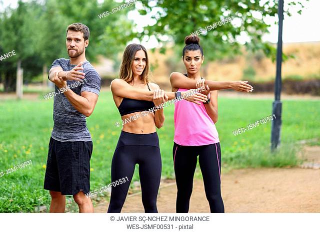 Young athletes doing shoulder stretches in a park