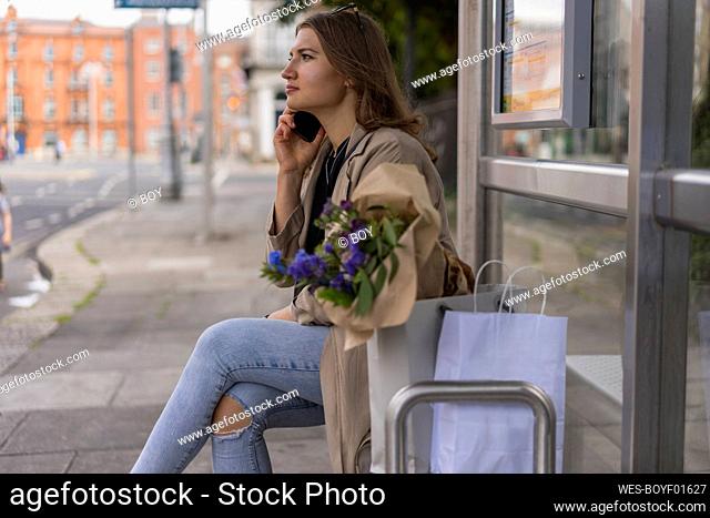 Young woman talking on smart phone while sitting in city