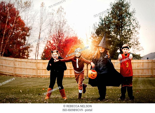 Portrait of boy and girls posed in halloween costumes in garden at sunset