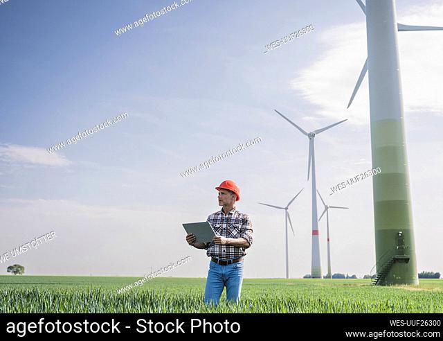 Engineer with digital tablet standing near wind turbine on sunny day