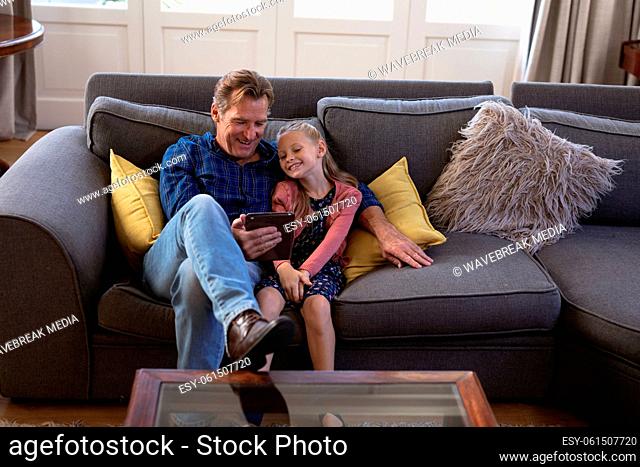 Caucasian girl and her grandfather spending time together at home sitting on a couch And using digit