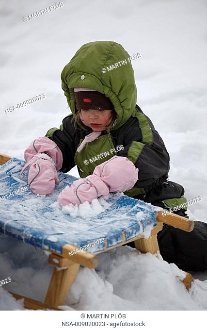 little girl playing with snow on toboggan