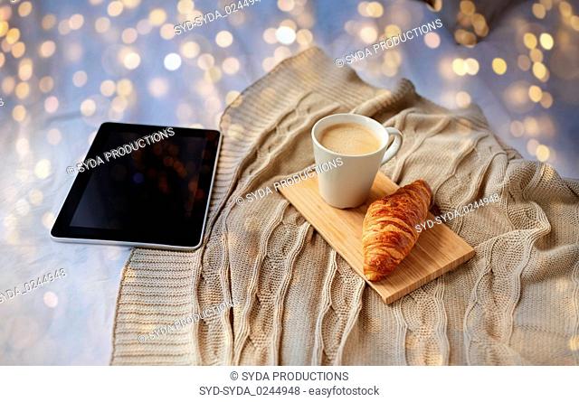 tablet pc, coffee and croissant on bed at home