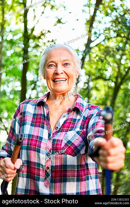 Fröhliche sportliche Seniorin beim Nordic Walking in der Natur im Sommer
