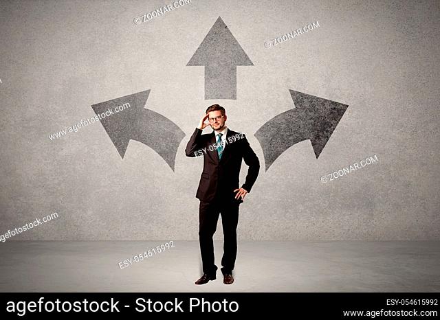 Charming businessman in doubt, choosing from three directions in front of a grey wall