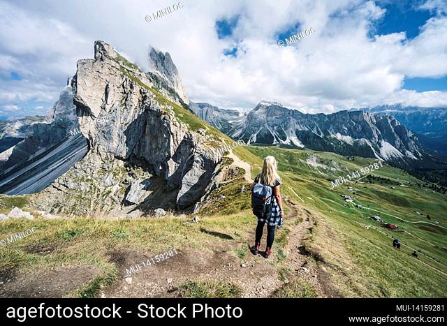 women hiker on hiking trail path and epic landscape of seceda peak in dolomites alps, odle mountain range, south tyrol, italy, europe