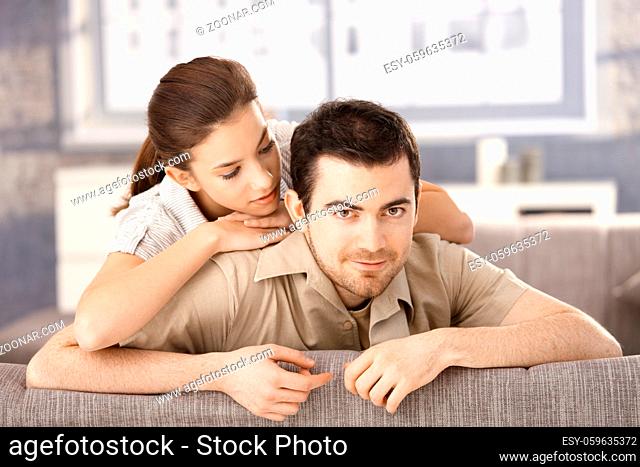 Happy couple sitting on sofa at home, hugging each other, smiling