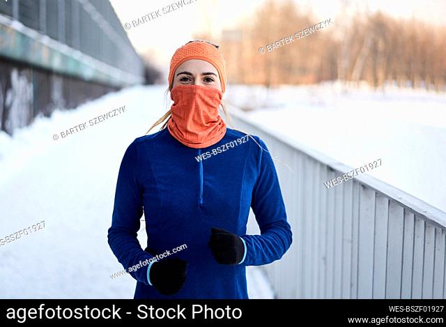 Young woman in gaiter face mask near railing during winter