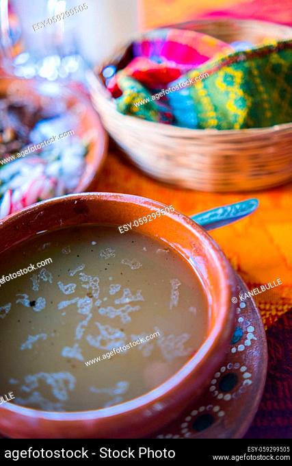 Close-up of clay bowl of lamb broth and tortilla basket on beautiful orange and red tablecloth. Traditional soupy dish and accompaniments above colorful table