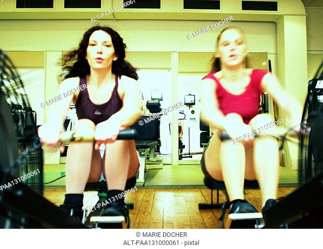 Women using rowing machines in gym, front view