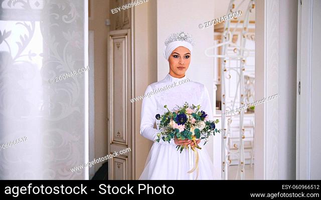 Portrait of young muslim bride with professional make up in white dress with flowers, horizontal