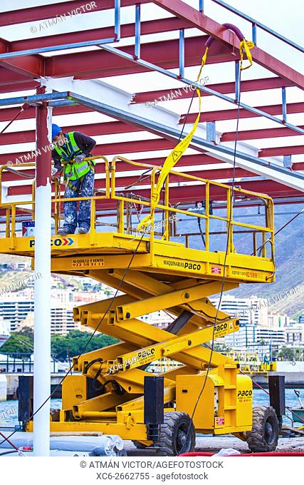 male painter working on a yellow lifting work platform beside a dock in Santa Cruz de Tenerife