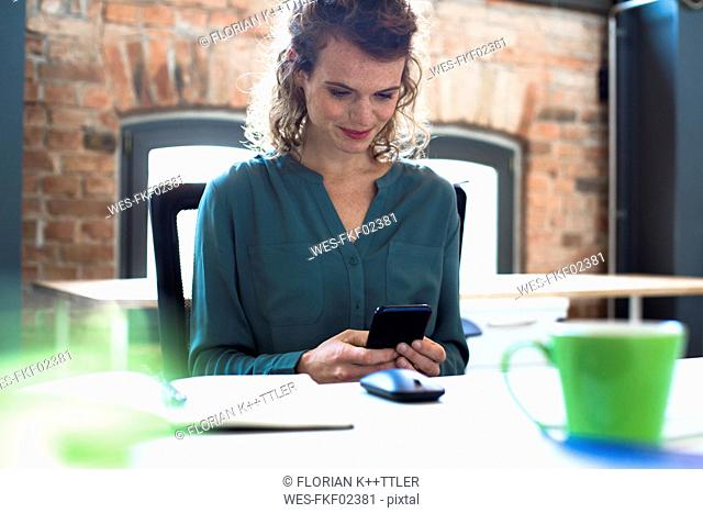 Young woman looking on cell phone at desk in office