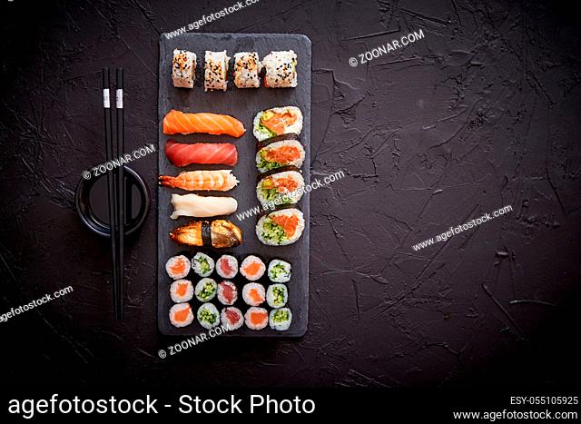 Sushi rolls set with salmon and tuna fish served on black stone board. Top view of traditional japanese cuisine. Asian food on black stone slate with chopsticks