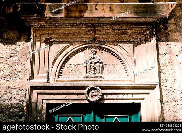 Entrance with green doors and bas-reliefs above them with the image of the saint and the crucifix. High quality photo